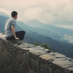 man on wall looking down on landscape