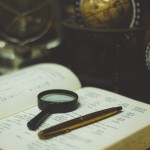 magnifying glass and pen on book in front of globes