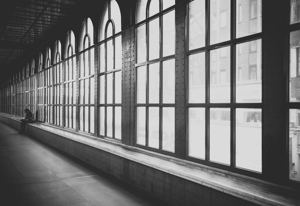 decorative image: figure sitting near bank of window, grayscale